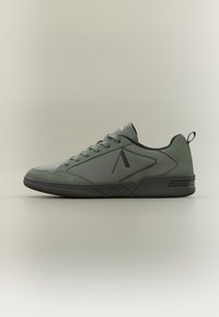 Green athletic shoes featuring leather and textile, a low-profile design, black rubber sole, and subtle logo detailing on the side.