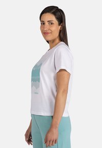 Camiseta de algodón blanca con mangas cortas, que presenta un gráfico de montaña azul y el logo de la marca impresos en el frente. Corte relajado y cuello redondo.