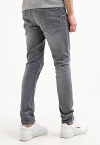 Vaqueros de mezclilla gris de ajuste ajustado con textura desteñida, diseño de cinco bolsillos y detalles sutiles de costura, combinados con zapatillas deportivas blancas.