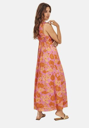 Vestido maxi en rosa con patrón floral naranja, diseño sin mangas y cintura fruncida. Modelo lleva sandalias y se muestra de perfil.