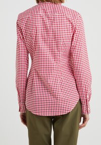 Červená a bílá kostkovaná košile s dlouhými rukávy, s límcem na knoflíky a přiléhavým střihem. Obsahuje zakřivený lem a knoflíky na manžetách.