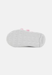 Suela de zapato deportivo blanca con una superficie texturizada, que presenta una banda de rodadura con un patrón para mayor agarre y un prominente logo de Adidas en el lateral.