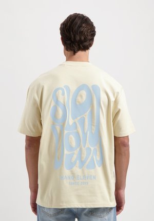 Lichtgeel t-shirt met op de achterkant een grote blauwe tekstgrafiek met de tekst "SLOW DOWN", met een casual pasvorm en een zachte textuur.