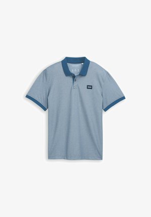 Gai zils polo krekls ar vienkrāsainu tumši zilu apkakli, īsām piedurknēm un mazu auduma etiķeti uz krūtīm, izgatavots no teksturēta kokvilnas materiāla.