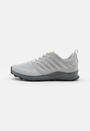 Chaussure de sport gris clair avec bout en mesh, design à lacets, semelle noire texturée, et boucle de traction sur le talon, sur fond blanc.