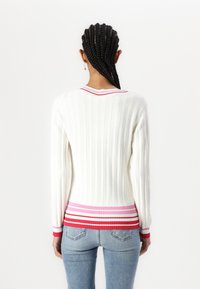 Maglione bianco a coste con colletto rotondo, presenta un orlo multicolore a righe in rosso, rosa e bianco. Maniche lunghe con dettagli testurizzati.