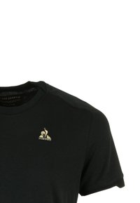 T-shirt noir à col rond avec un petit logo doré Le Coq Sportif sur la poitrine gauche.