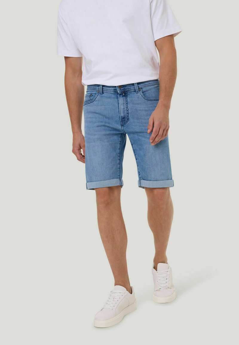 Shorts en denim bleu clair avec des revers, design à cinq poches et coupe standard, associés à un t-shirt blanc uni et des baskets blanches.
