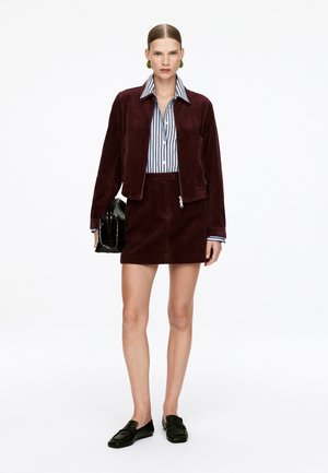Burgundy corduroy jacket with matching short skirt, blue and white striped shirt underneath, paired with black loafers and a black handbag.