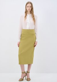 Bílá blůzka s řaseným předním dílem, spárovaná se středně dlouhou olivově zelenou tužkovou sukní. Celý outfit doplňují sandály na vysokém podpatku s řemínky.