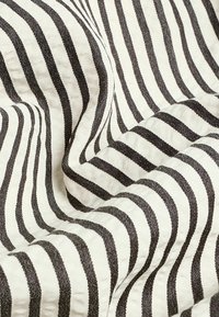 Tissu blanc avec des rayures verticales noires, présenté avec des plis et des détails de texture.