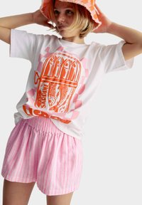Witte T-shirt met een oranje sardine-graphic en roze accenten, gecombineerd met lichte roze en witte gestreepte shorts met een elastische tailleband.