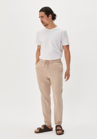 Light beige elastic waist pants paired with a fitted white t-shirt and black slide sandals. Simple design, smooth texture, and comfortable fit.