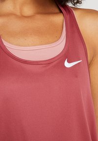 Gros plan sur une personne portant des débardeurs de sport roses superposés avec un logo Nike blanc sur le débardeur extérieur.