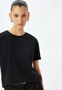 Zwart katoenen t-shirt met korte mouwen en een ronde halslijn. Kenmerkt een subtiele reliëftekst: "Accepteer jezelf, accepteer anderen."
