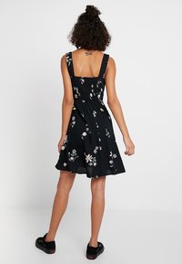 Robe noire à fleurs avec un corsage ajusté et smocké et des bretelles larges ; dotée d'une jupe évasée ornée de motifs floraux multicolores.