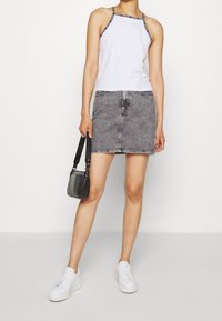 Canottiera bianca con bordi neri, gonna in denim grigia, sneakers bianche e una piccola borsa nera in pelle di coccodrillo.