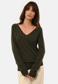 Tmavě zelený svetr s jemnou texturou, V-výstřihem a dlouhými rukávy. Přiléhavý střih s žebrovanými manžetami a lemem.