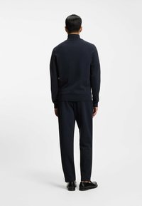 Ensemble de sweat-shirt et pantalon bleu marine, avec un col haut, des poignets et un ourlet côtelés. Texture lisse avec une coupe décontractée. Des chaussures noires complètent le look.