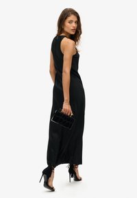 Robe noire sans manches au design ajusté, ornée d'un accent doré à l'arrière. Associée à une pochette noire texturée et des chaussures à talons hauts.