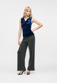 Blå fløyels uten ermer topp med en cowl hals, kombinert med vide svarte mønstrede bukser og svarte åpen-tå hæler.