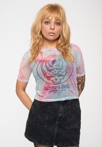 Sheer, short-sleeve top in pastel colors with a Grateful Dead skull graphic; paired with a black denim skirt featuring front pockets.