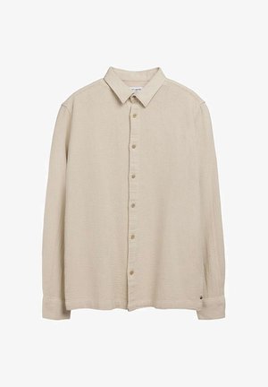 Chemise beige à manches longues, boutonnée, en tissu texturé avec col classique, étalée à plat sur un fond blanc.