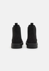 Botines de ante negro con caña alta, que presentan lados texturizados, tiradores y una suela de goma suave. Diseño sencillo sin hardware visible.