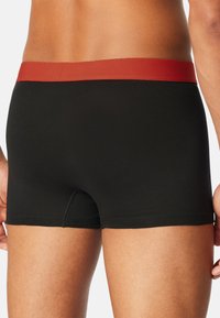 Czarne bokserki z czerwonym elastycznym pasem, charakteryzujące się gładką fakturą i obcisłym krojem. Widoczne przeszycia i krótka długość.