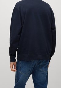 Felpa blu navy con scollo rotondo e polsini a costine, abbinata a jeans blu sbiaditi. Tessuto morbido con dettagli minimi.