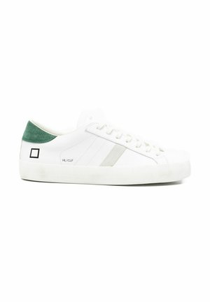 Sneaker bianca basse con linguetta sul tallone in suede verde, strisce laterali grigie e logo quadrato nero vicino al tallone su suola bianca.
