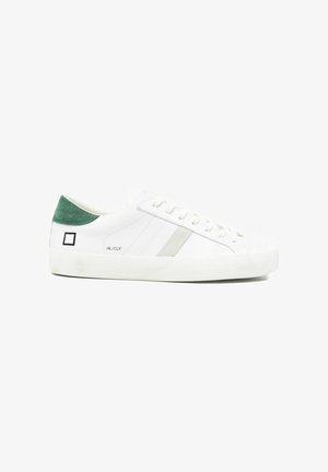 Sneaker bianca basse con linguetta sul tallone in suede verde, strisce laterali grigie e logo quadrato nero vicino al tallone su suola bianca.