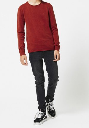 Czerwony sweter z długimi rękawami i okrągłym dekoltem, połączony z ciemnymi dżinsami oraz czarnymi wysokimi trampkami z białymi sznurowadłami i detalami.