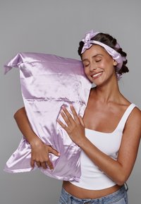 Taie d'oreiller en soie de couleur lavande claire, texture lisse, tenue de près, accompagnée d'un bandeau en tissu assorti avec un détail en nœud.