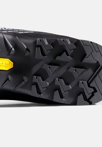 Schwarze Gummisohle mit ausgeprägtem Profildesign, das winklige Stollen und ein gelbes Vibram-Logo für verbesserte Traktion und Haltbarkeit beinhaltet.