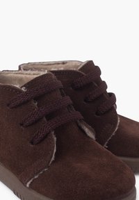 Botas de cuero ante marrón hasta el tobillo con cierre de cordones, forro suave, punta redondeada y suela texturizada. Presenta costuras visibles y acentos de felpa.