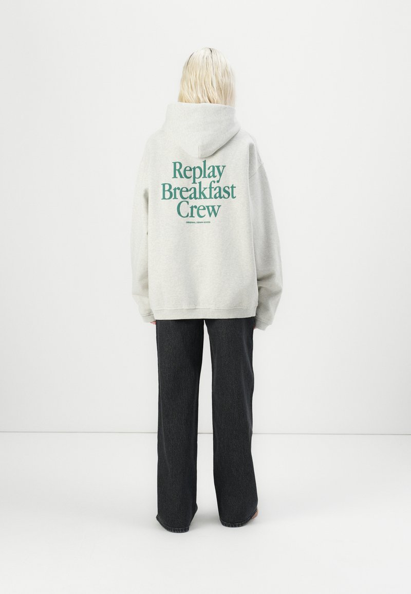 Light gray hoodie with "Replay Breakfast Crew" printed in dark green on the back. Paired with dark denim pants. Soft fabric, loose fit.