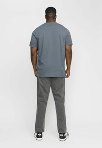 Grå kortærmet t-shirt, stofblanding af bomuld, lige pasform. Kombineret med grå bukser og sorte sneakers med hvide såler. Minimalistisk design.