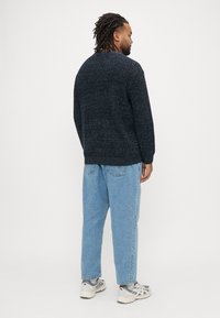 Tamsiai mėlynas tekst�ūruotas megztinis su apvaliu kaklu, derinamas su šviesiai mėlynais laisvo kirpimo džinsais ir pilkais sportbačiais, matomas iš nugaros.