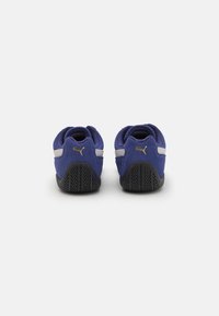 Blå semskede sneakers med sorte gummisåler, der har sølvstriber og et guld logo. Rund hæl og struktureret ydersål for godt greb.