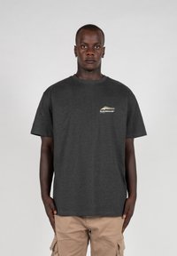 Tricou gri închis din bumbac. Mâneci scurte, guler rotund, prezintă un mic logo alb și auriu în zona pieptului stâng.