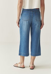 Blue denim culotte jeans with a high waist, cropped length, and frayed hem. Features two back pockets and a smooth texture.