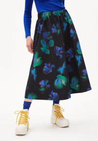 Jupe noire avec des motifs floraux vibrants verts et bleus, une taille élastique, associée à des baskets montantes blanches avec des lacets jaunes.