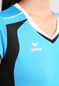Blaues Sporttrikot mit schwarzen Akzenten, V-Ausschnitt, kurzen Ärmeln und weißem Logo "erima" auf der Vorderseite. Glatter, atmungsaktiver Stoff.