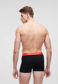 Caleçons boxers noirs avec une taille rouge, portant le texte "MERCREDI" et "KARL LAGERFELD". Tissu doux avec un design ajusté.