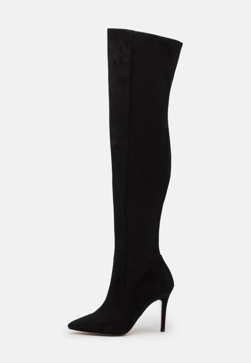 Bota de tacón stiletto negra por encima de la rodilla, con punta afilada y material de ante suave, exhibida sobre un fondo blanco.