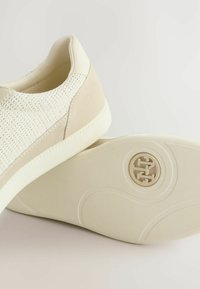 Zapatillas beige con parte superior de malla texturizada, acentos de ante suave y una suela de goma con un logotipo circular en el talón.