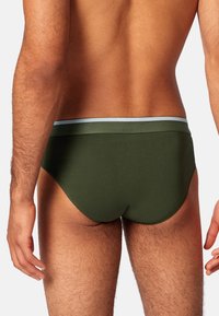 Donkergroene herenonderbroek gemaakt van zacht materiaal. Voorzien van een lichtblauwe tailleband en een getailleerd ontwerp, dat de vorm en pasvorm benadrukt.