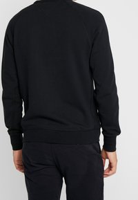 Sort sweatshirt med ribbet halsudskæring og manchetter. Glat tekstur med synlige syningsdetaljer langs sømmene.