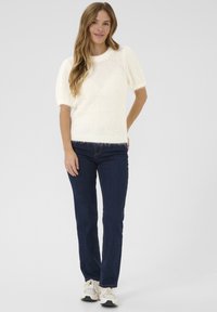 Pull côtelé couleur crème avec des manches courtes bouffantes, associé à un jean bleu foncé et des baskets blanches. Tenue simple et décontractée.